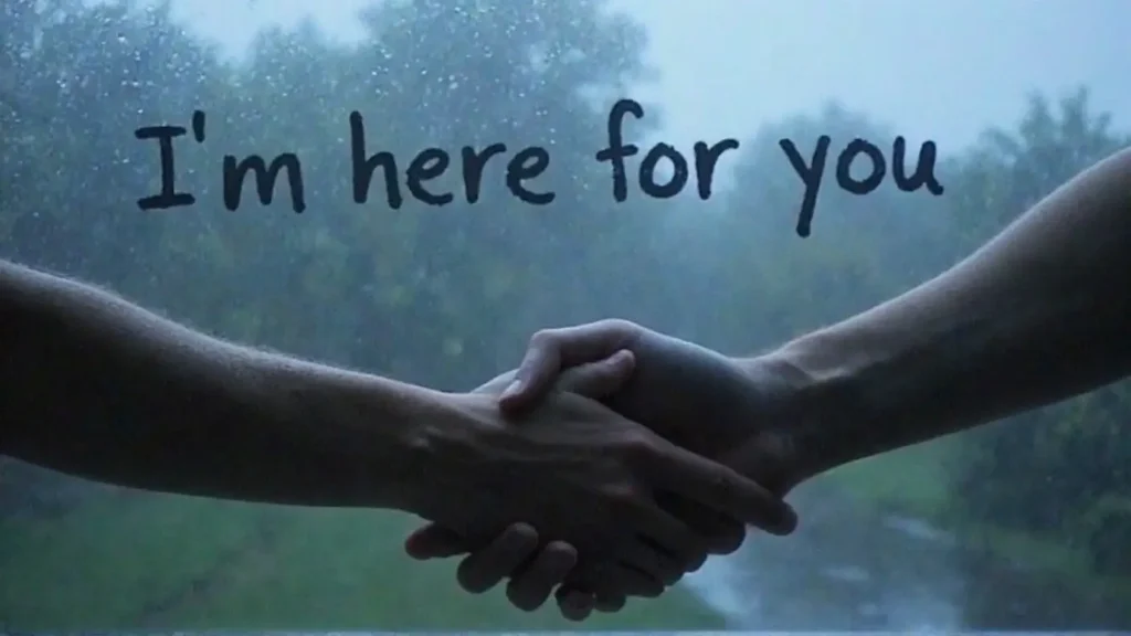 Two hands interlocked, symbolizing support, with the emotional message "I'm here for you" written on a steamy window in the background.
